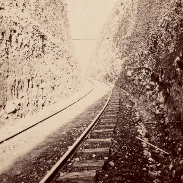 Faded black and white photo of train tracks running through a narrow canyon.