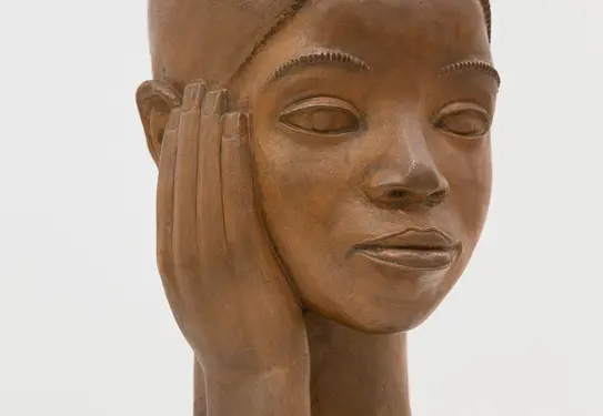 sculpture of wooden head with hand on side of face