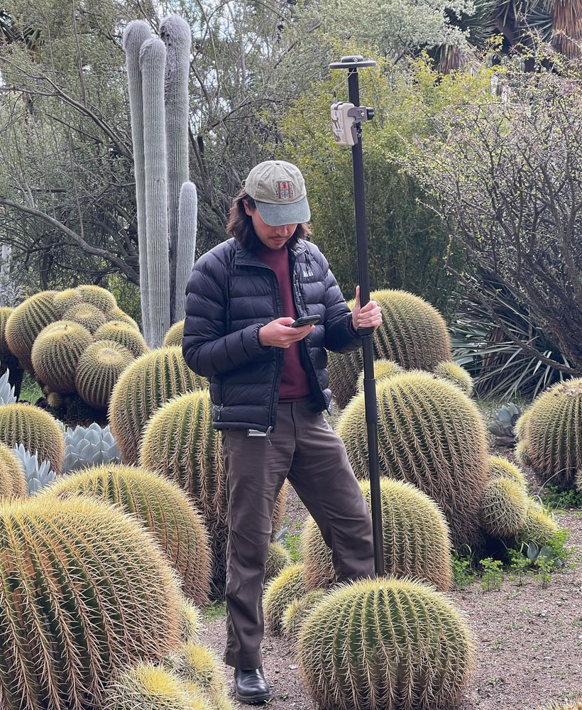 A person stands with mapping equipment, surrounded by cacti.