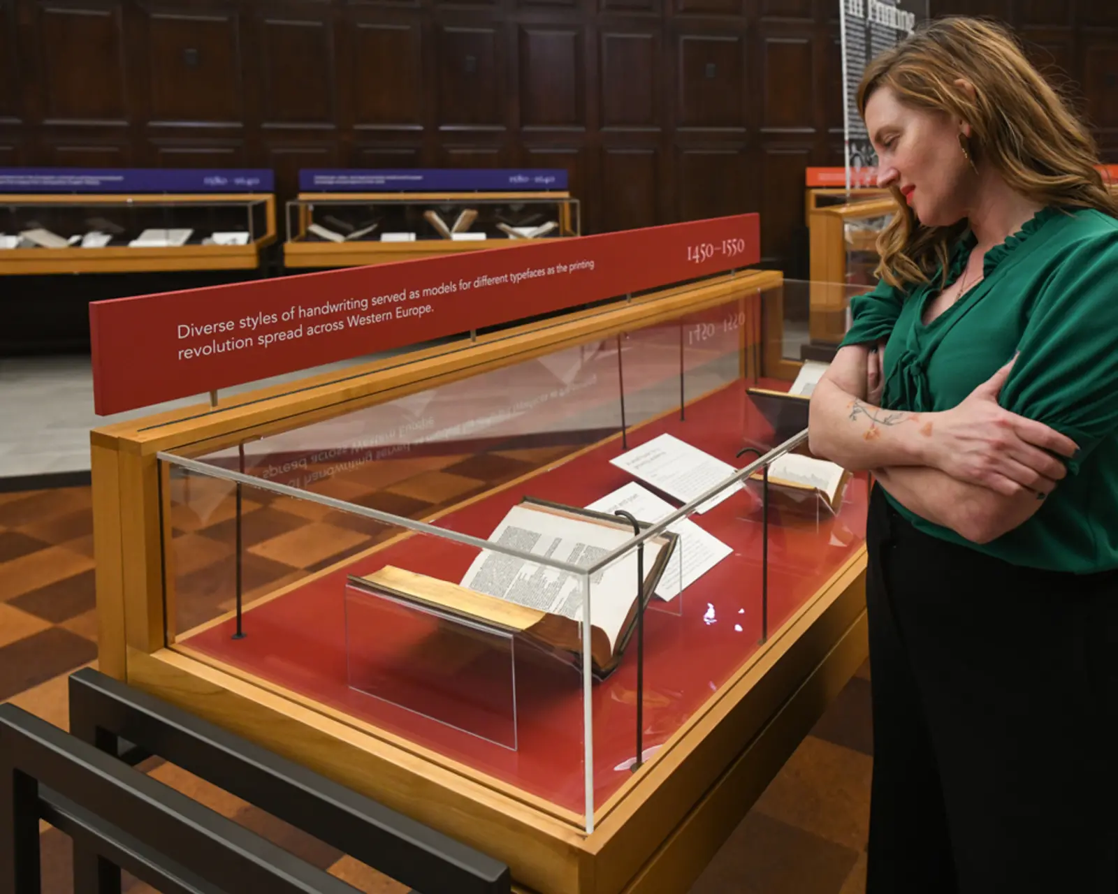 A person looks at a book in a glass case in a library.