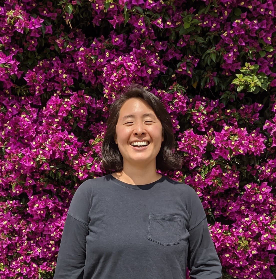A woman with short brown hair smiling in front of a wall covered with bougainvillea
