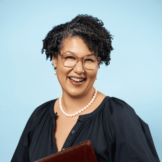 A smiling person with short curly hair and glasses.