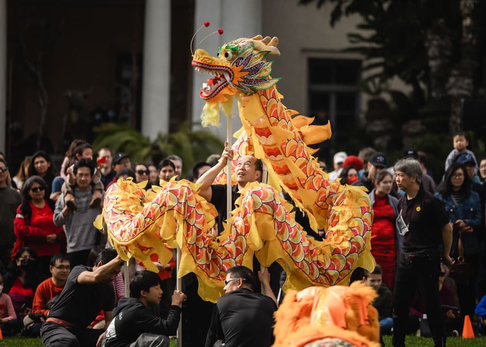 A crowd of people watch a yellow dragon puppet.