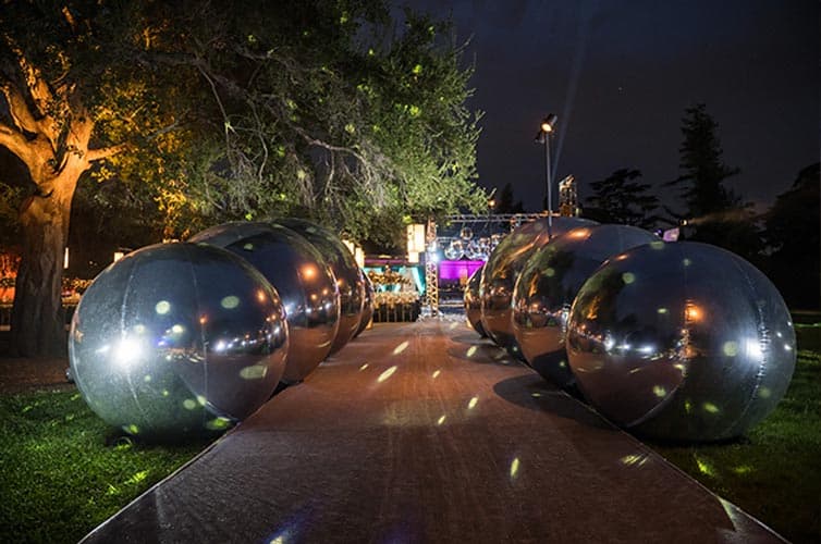 A sidewalk at night adorned by large silver globes on either side.