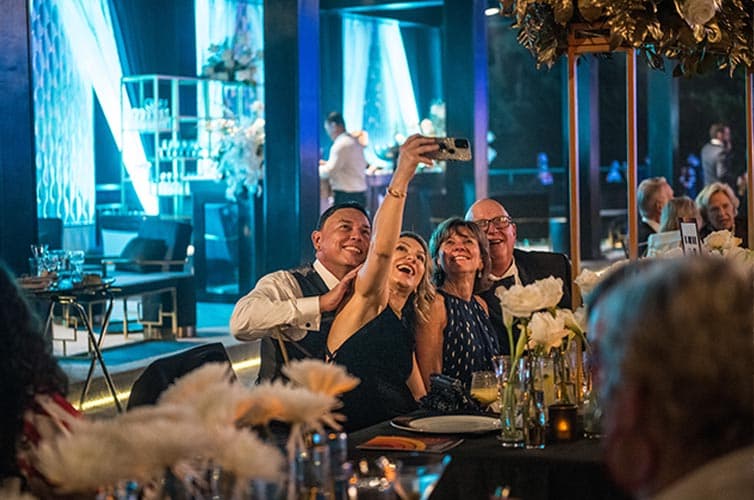 People take a selfie while seated at an outdoor dining table.