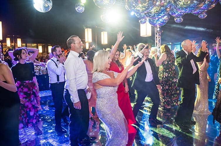 A person raises their hands in the air while dancing with others on an outdoor dance floor.