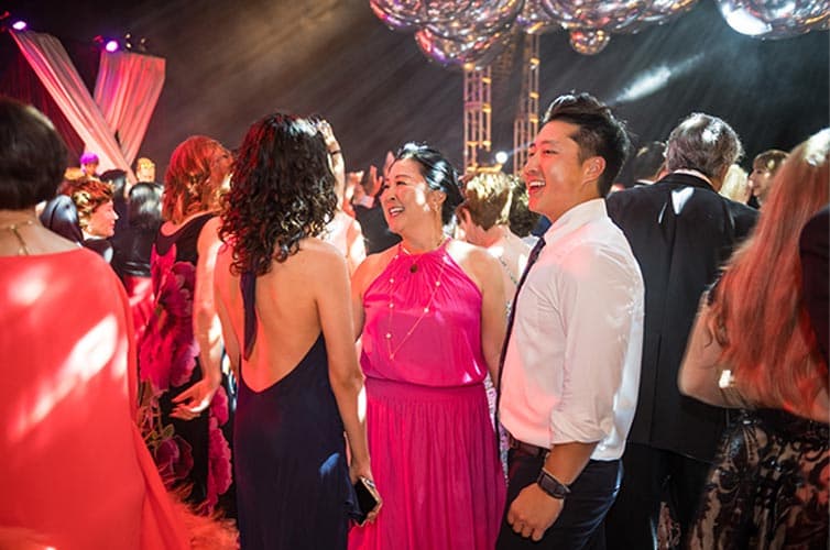 People dressed in evening wear laugh while on a dance floor.