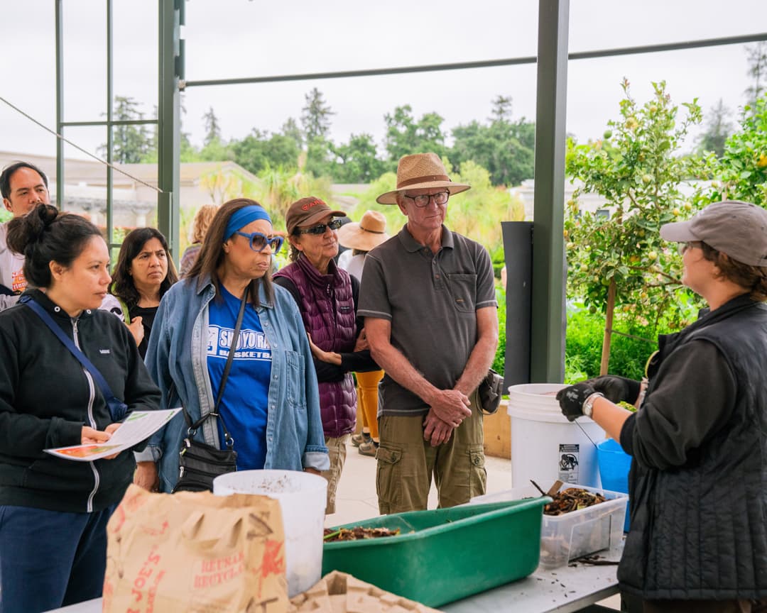 A group of people listen to a speaker in a garden.