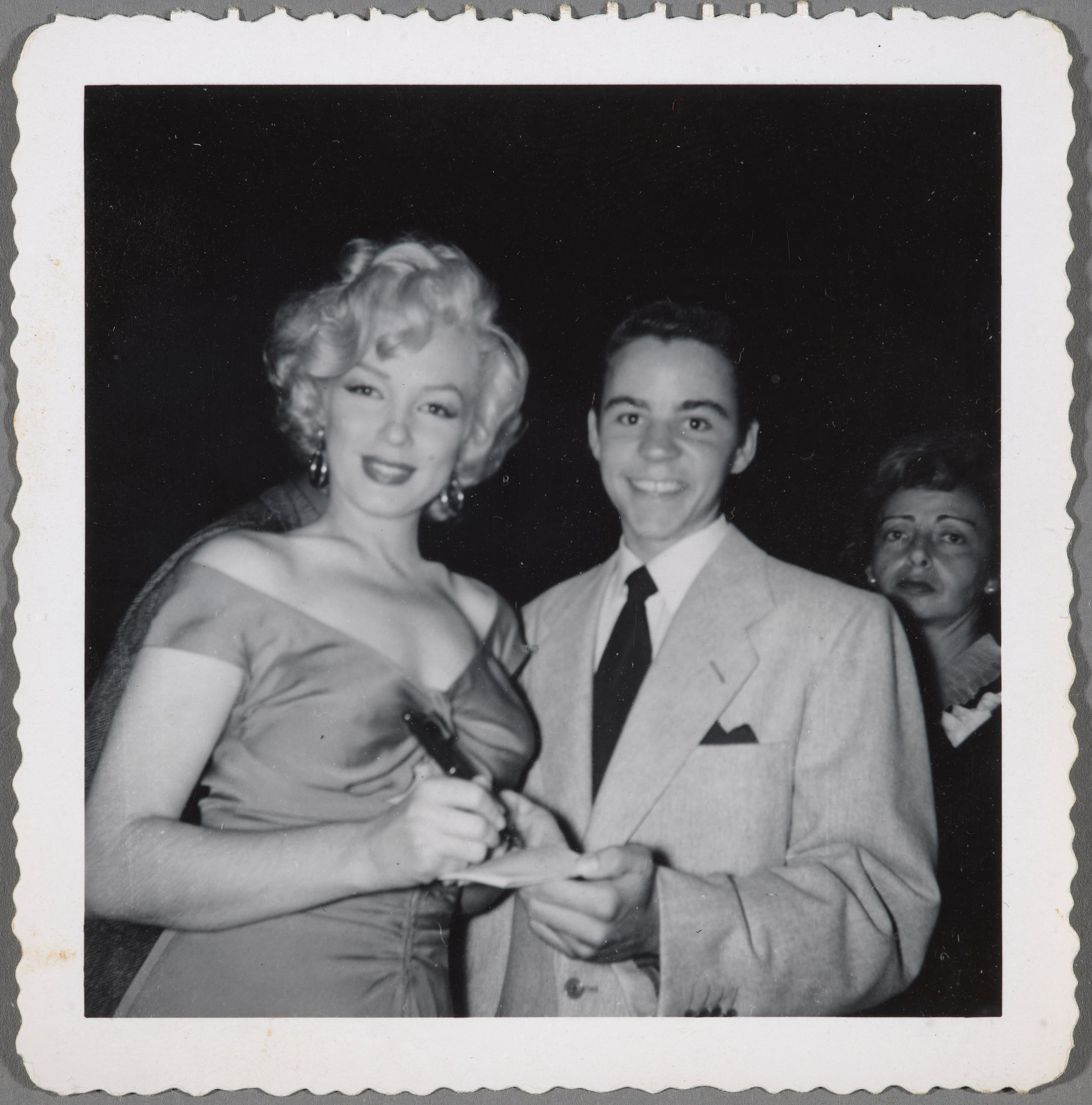 A black-and-white photo of a young man in a suit getting an autograph from Marylin Monroe.