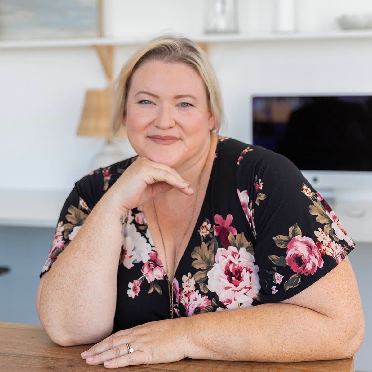 A person in a flower top poses for the camera in an office setting.