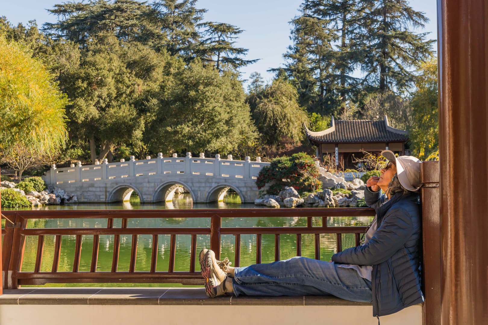 A person sits on a bench near a lake in a Chinese garden.
