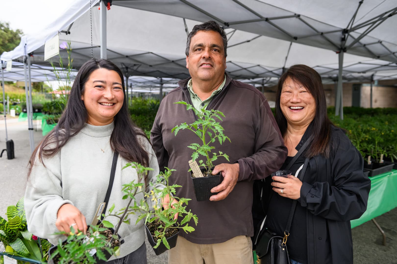 Three smiling people holding potted plants.