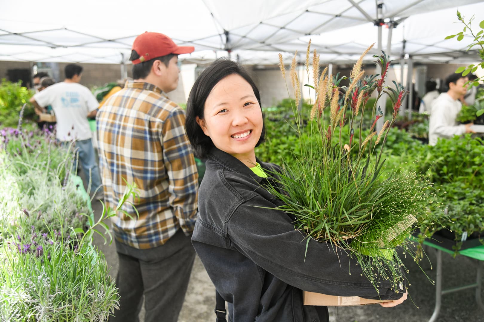 A smiling person holds an arm-full of potted plants.