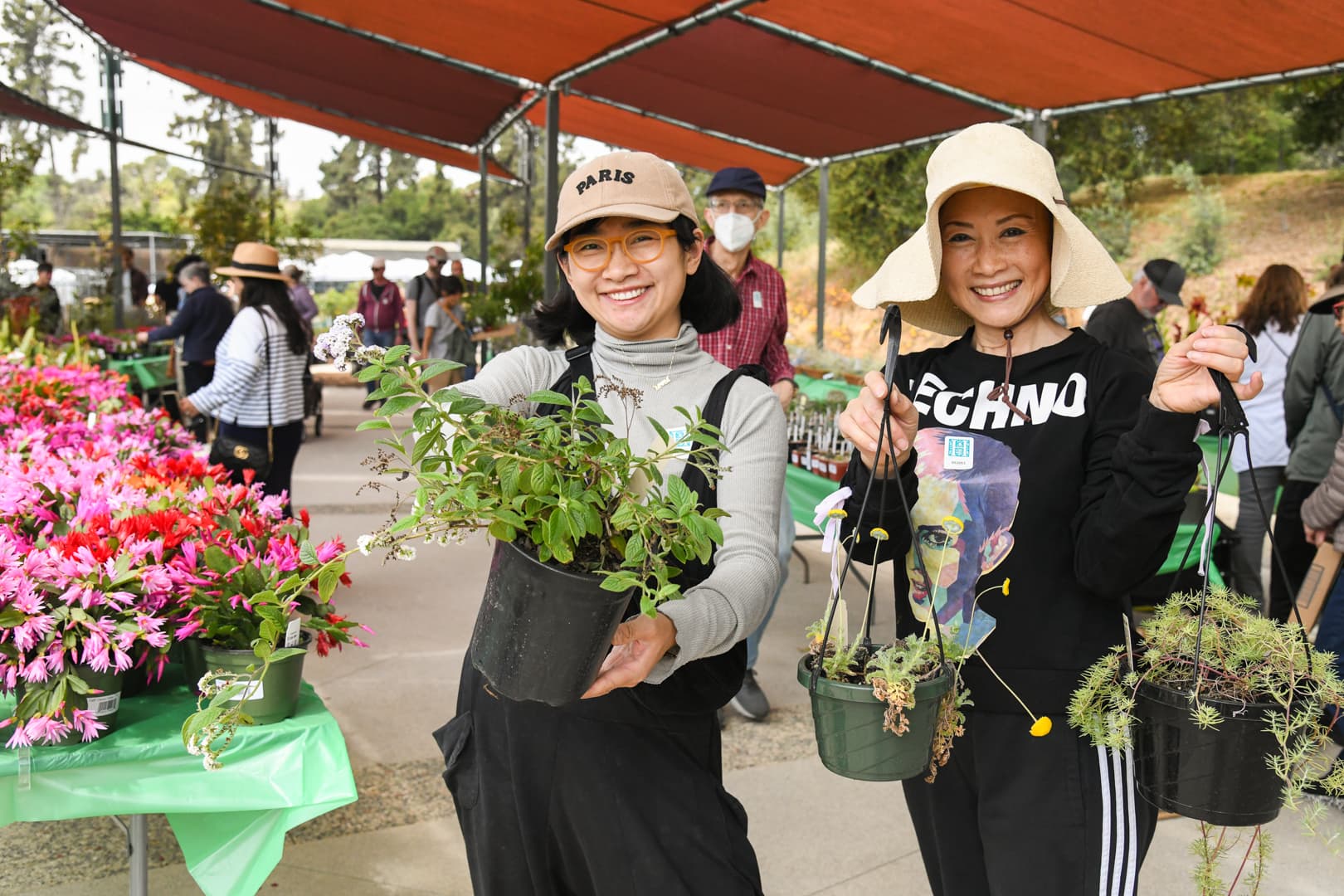 Two smiling people hold up potted plants.