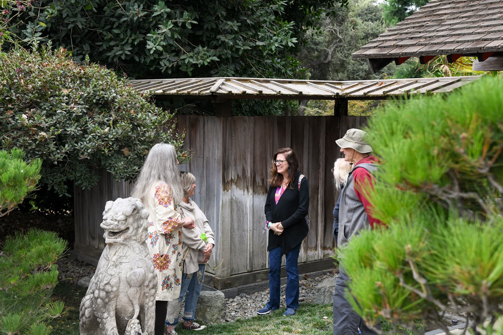 A group of people stand near a wooden wall in a Japanese-style garden.