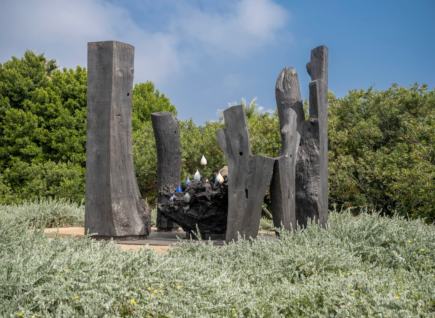 A wood sculpture in a garden, with ceramic droplets at the center.