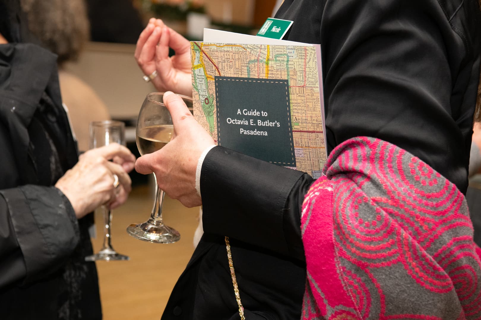 A person holds a printed brochure and a glass of white wine.