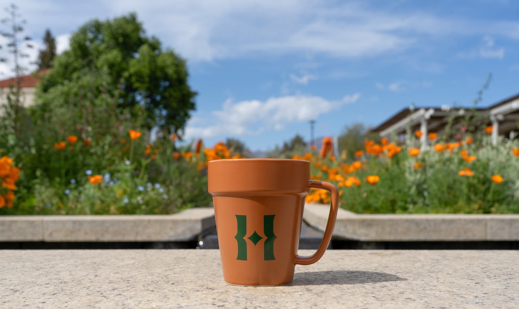 A mug with a green H logo resembles a terra-cotta pot in a garden.
