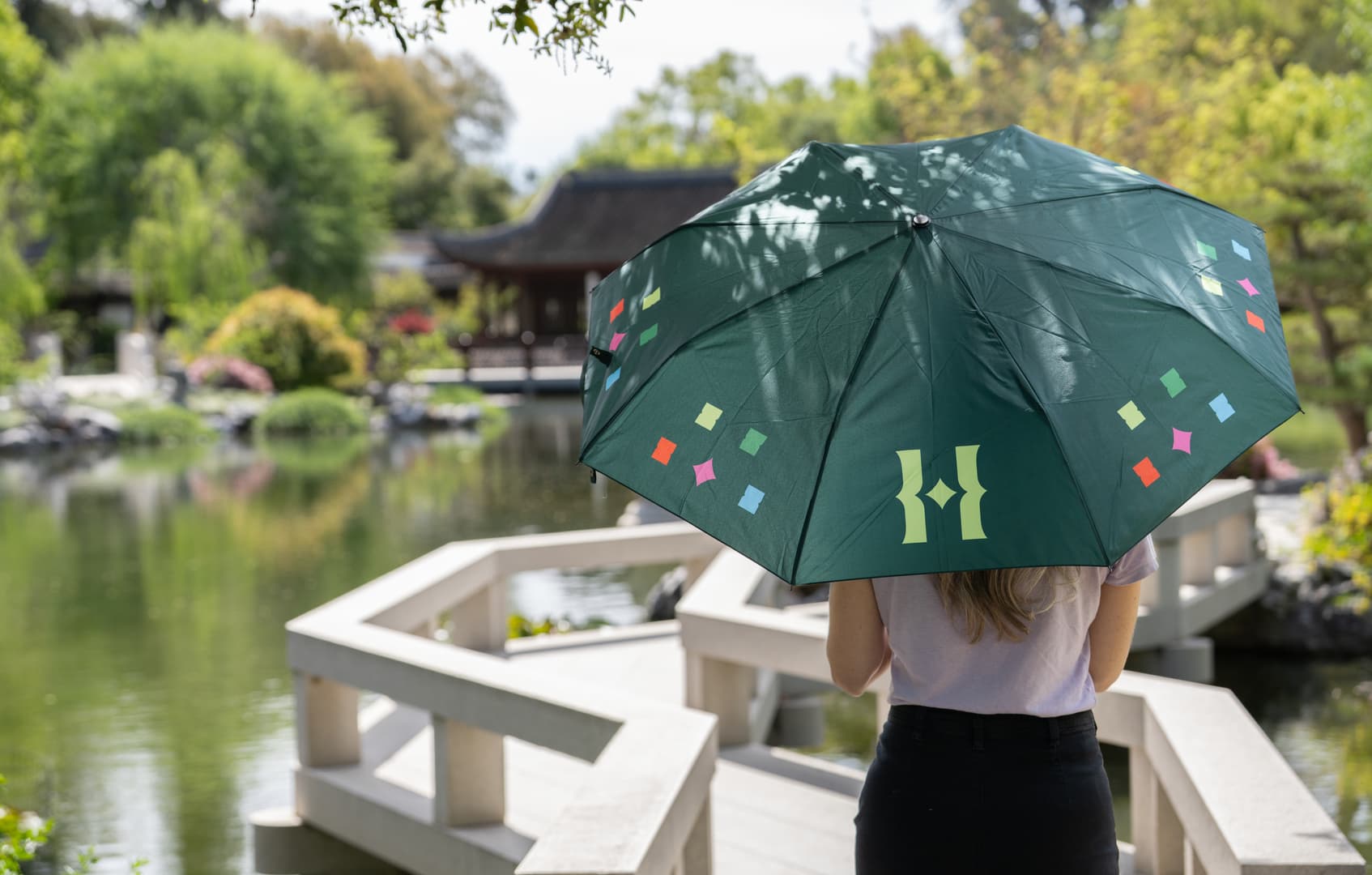 A person holds a green umbrella in a Chinese-style garden.