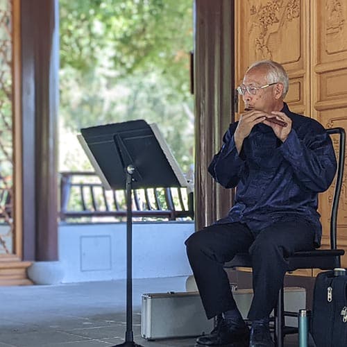 A person plays a flute in a garden.