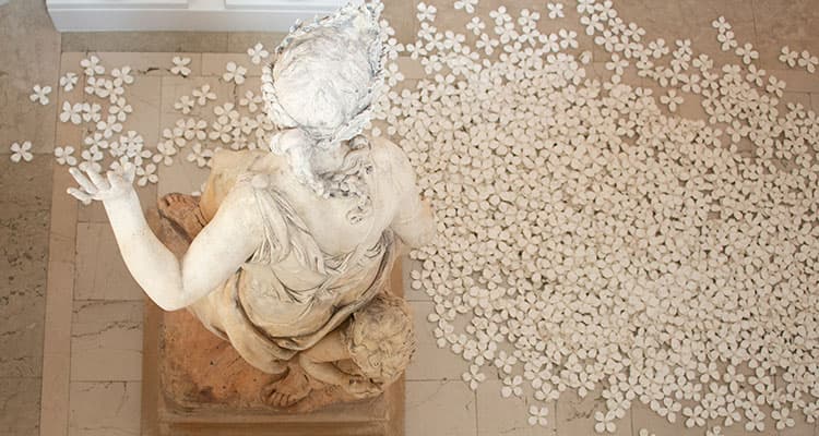An overhead view of a sculpture of a person, surrounded by ceramic flowers.
