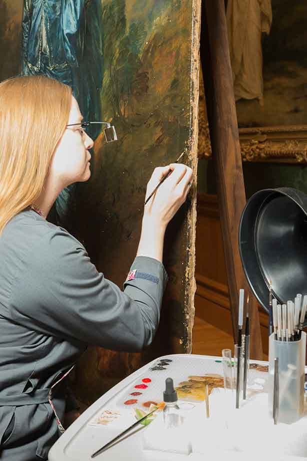 Closeup view of Christina Milton O’Connell, Mary Ann and John Sturgeon Senior Paintings Conservator, using tiny brushes to reconnect Gainsborough’s brushstrokes across the voids of past damages. The Huntington Library, Art Museum, and Botanical Gardens.