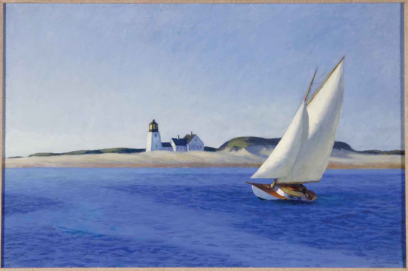 A leaning sailboat sits in calm deep-blue waters not far from a sandy beach and lighthouse.