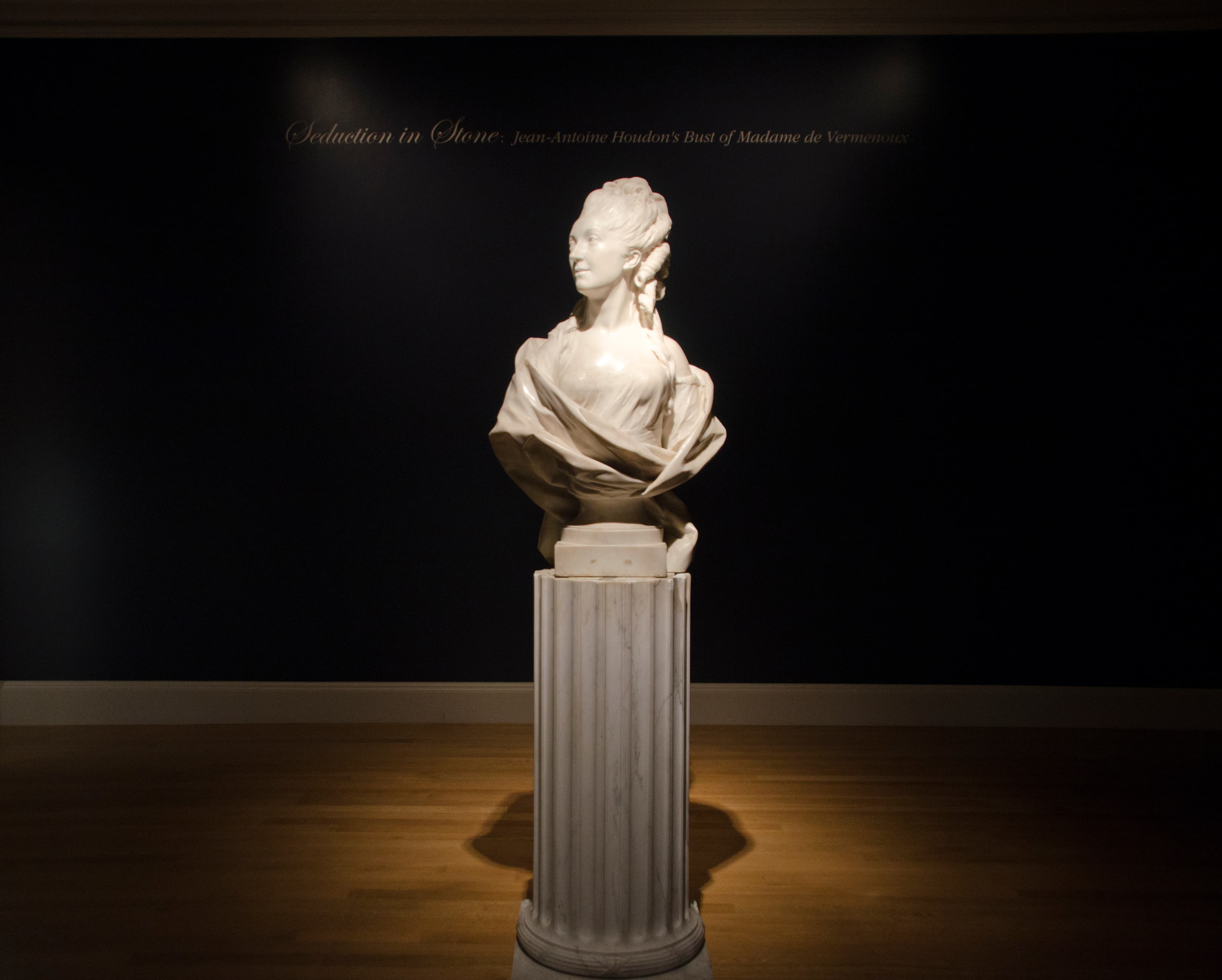 A marble statue of a woman with long, flowing, curly hair, looks to the side.