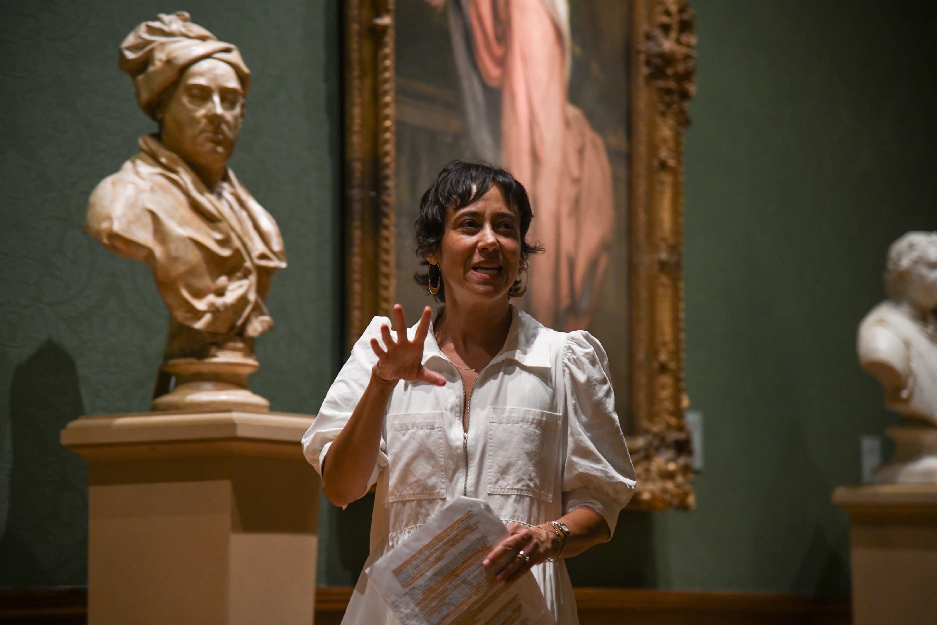A person stands in front of a head bust in a gallery space.