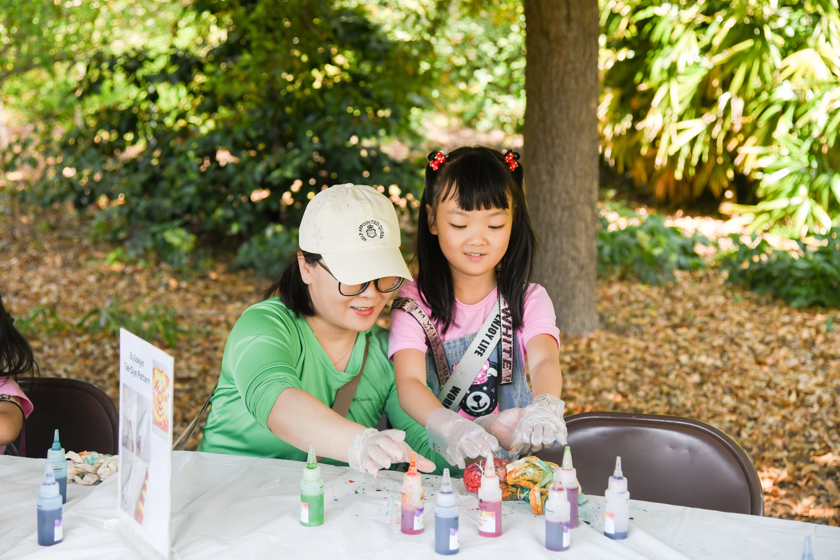 An adult helps a child pick out bottles of various tie-dye paint colors.