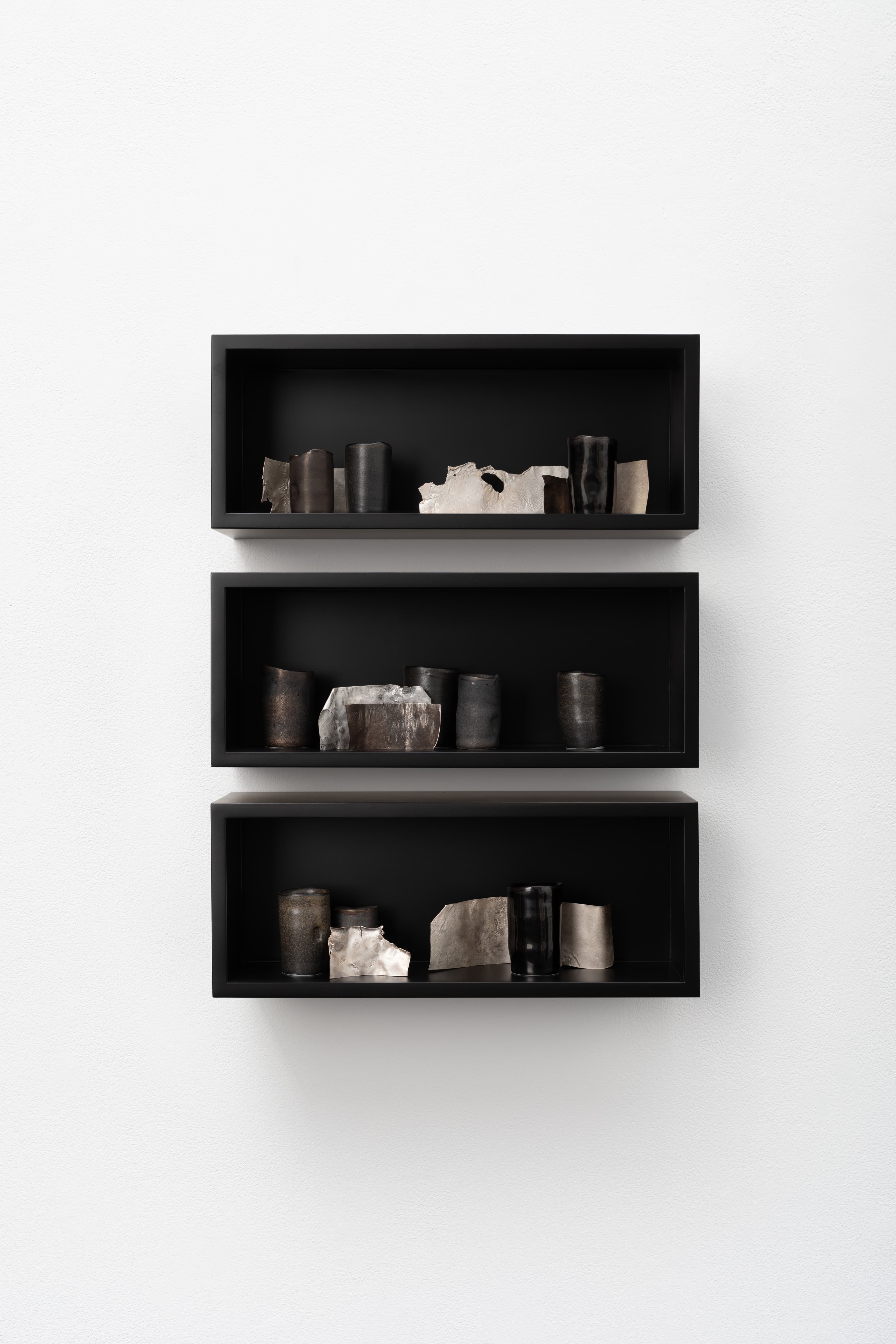 Three black, wall-mounted shelves display objects.