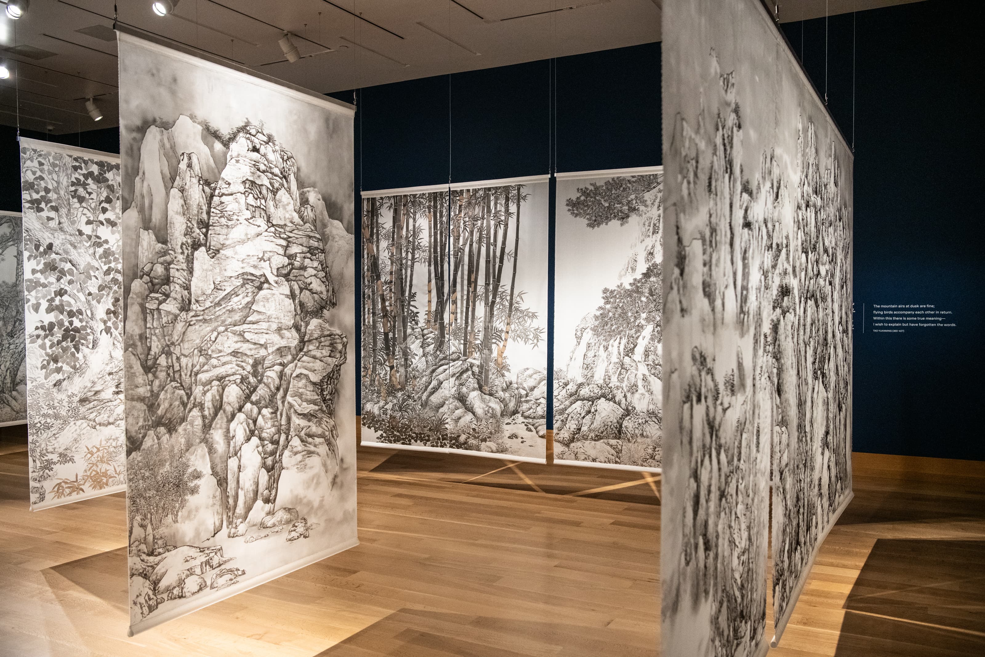 4 silk panels with hand-painted drawings of rocks and trees hang in a gallery.