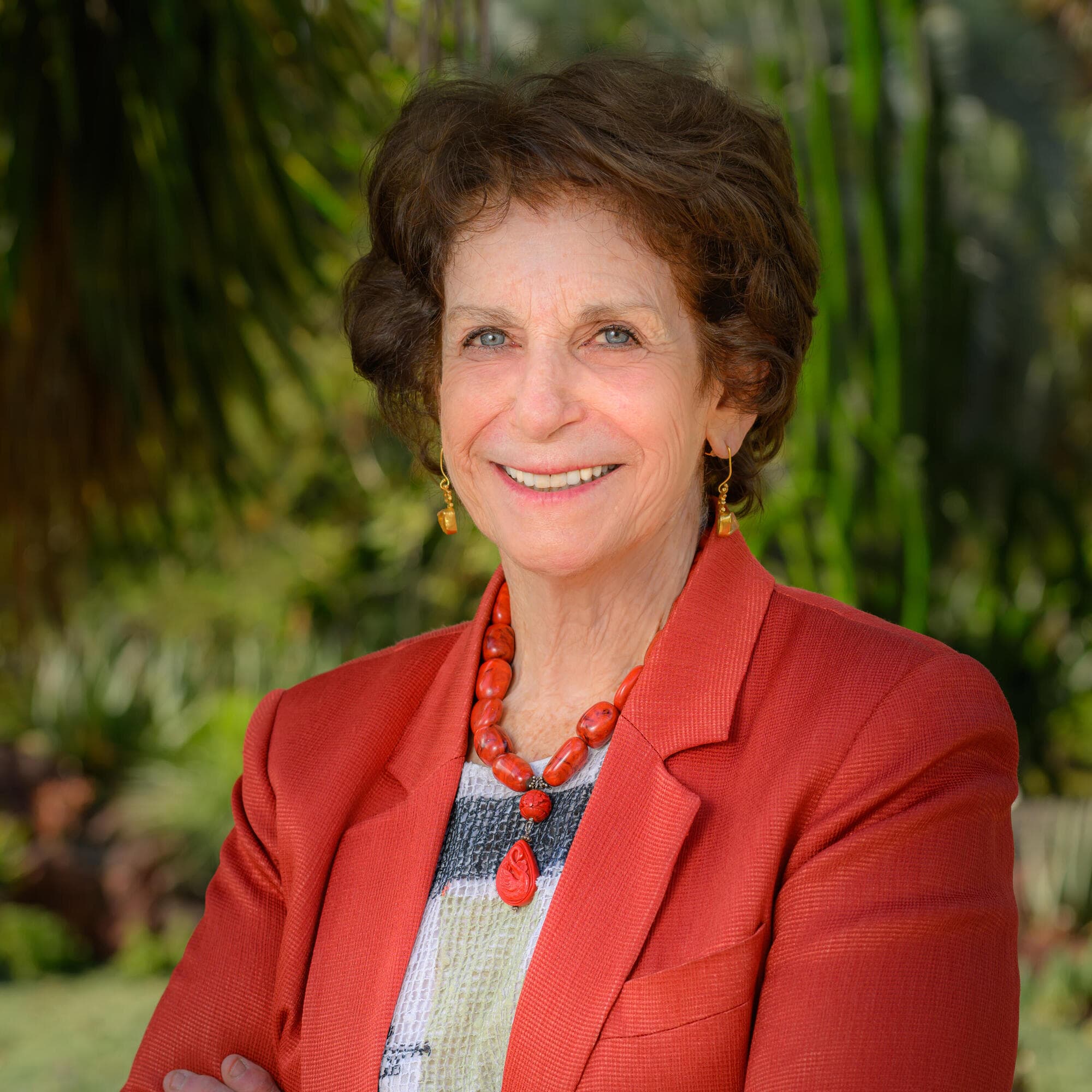 Person in a terracotta blazer standing outdoors with arms crossed.