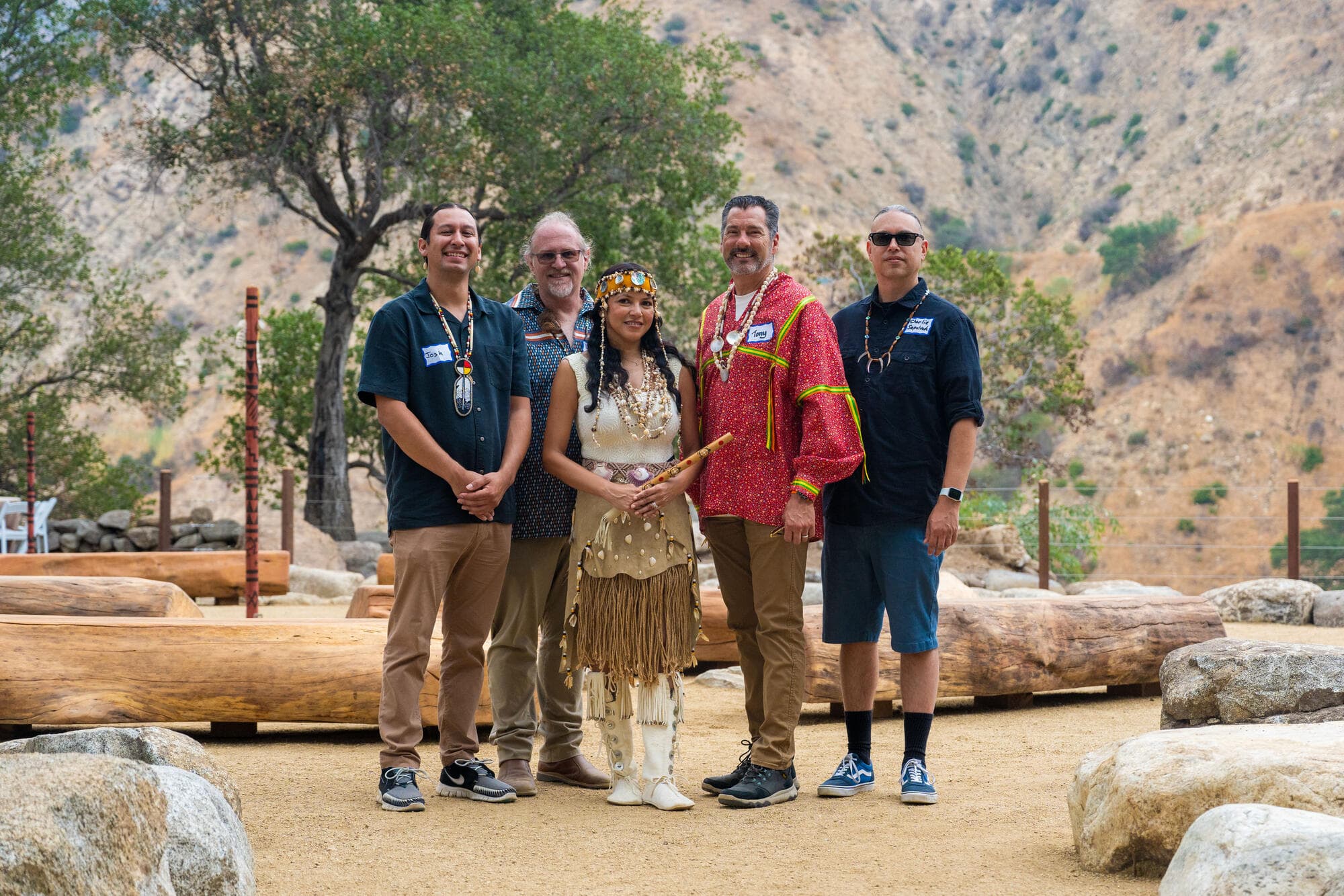  Four men and one woman in traditional Tongva Native American clothing by a ceremonial circle.