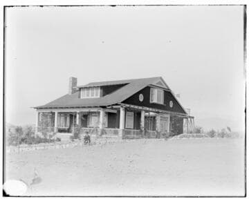 A man in a suit with a bowler hat sitting in front of Arts & Crafts home