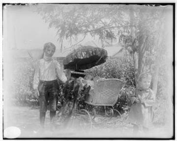 Two young boys standing next to a stroller with a baby