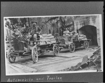 Three men riding in an automobile and trailers for hauling cement during the construction of the flowline at Kern River #1 Hydro Plant