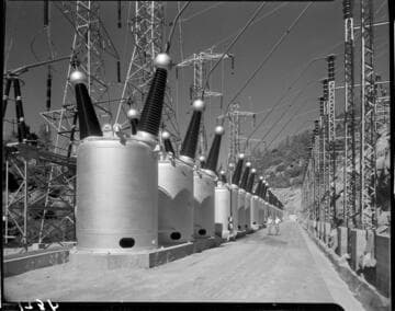 Two men talking halfway down a long bank of huge circuit breakers and other swichgear at Big Creek
