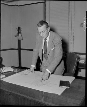 Man looking at land parcel map with a large lake spread out on is desk