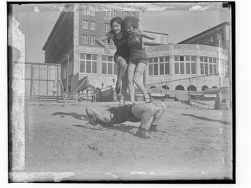 Two women standing on the torso of Henry Steinborn in front of Club Casa del Mar