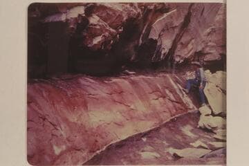 Red stains on rock at spring in Black Water Creek; North side of Navajo Mountain. Black Water Cave. Tom Daly in the background