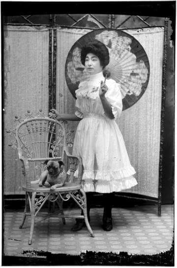 Portrait of a Chinese woman standing and holding parasol, with a small dog on a chair