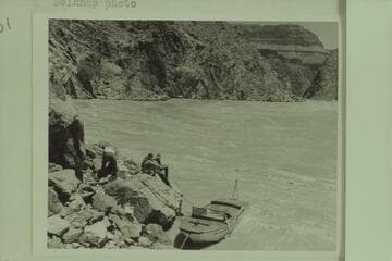 The "Esmeralda" pulled into the rocky shore of the eddy at the right bank at Mile 99.4.  Hudson is unloading equipment preparing to abandon the craft.  Guy Forcier and Edward Hudson watch from the bank.  Bright Angel gauge:  54,000 cfs