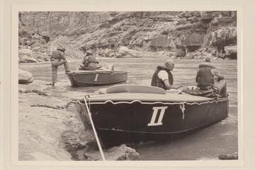 The two 18-ft. boats of the outboard fleet of the 1953 traverse of the Canyons. Bill Belknap sits on the I. Ed Ralph talks with Don Harris in the II. Note the boulder of Boulder Narrows in the background. Flow approximates 50,000 cfs