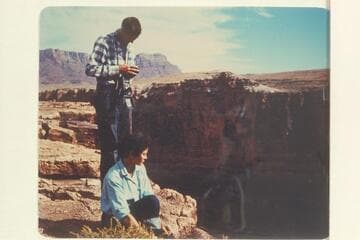 Susie Reilly sits at the edge of Marble Canyon looking down at Badger Creek Rapid. Pat Reilly prepares for photography