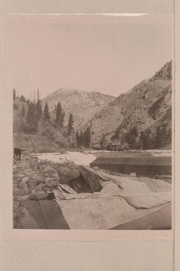 Carl Biedenbach in his bed on top of inflated boat. Don Smith's 30-ft. sweep scow in background rigged with cover