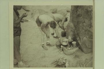 Breakfast at camp at Mile 19, right bank. Marston stands at left. Edward Hudson and Willie Taylor dish up the mix