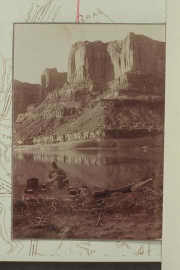 Camp below mouth of Hell Roaring Canyon. Taken during trip in 1901-1902 from Greenriver, Utah, to Rapid #3 in Cataract Canyon. Probably Arthur O. McCormick in the scene. The Wingate in the background is part of the Twin Fortress