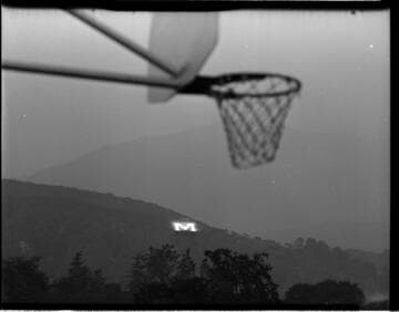 Illuminated "M" (Monrovia) on hillside with basketball hoop in foreground