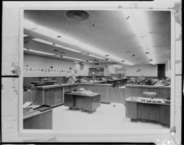 Office space with desks and partitions. Numbers are written at various points on the print used to make this negative